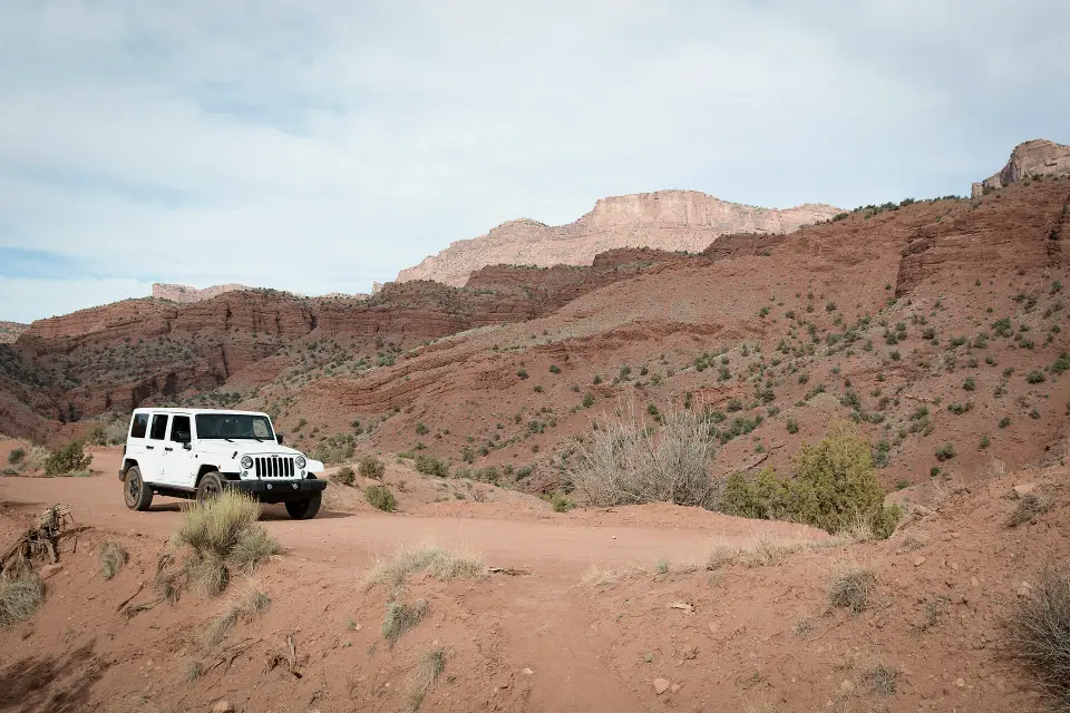 A white Jeep on a dirt track among red desert hills.